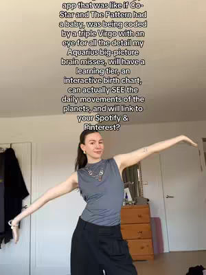 A woman with her arms outstretched, suggesting a pose of confident presentation, stands in a well-lit room. Behind her is a glimpse of domestic fittings: a door, a chest of drawers and a mirror. The background light suggests a casual or home environment.