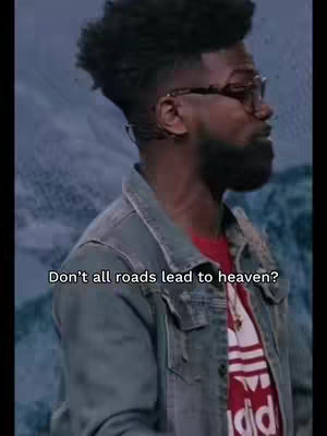 A man with glasses and a beard is seen from the chest up, positioned slightly off-center. He is wearing a red t-shirt with white stripes and the Adidas logo, layered under a denim jacket. The background has a blurred effect, suggesting an indoor setting with a light blue color palate. The text overlayed on the image questions, 'Don't all roads lead to heaven?'