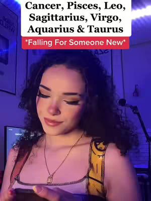 A young woman with curly dark hair, wearing a white top with a unique yellow-trimmed strap, looks down towards the lower portion of the frame, possibly holding a phone or other device. She has makeup which includes eyeshadow and a soft lip color. A decorative necklace hangs around her neck. A sign with white text on a red background is superimposed above her. The background fades from a deep blue to a lighter tone.