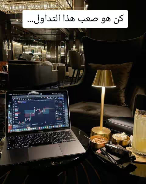 A laptop displaying a stock trading chart sits on a table in a dimly lit lounge setting. A lamp and snacks are nearby. The background shows a luxurious interior.