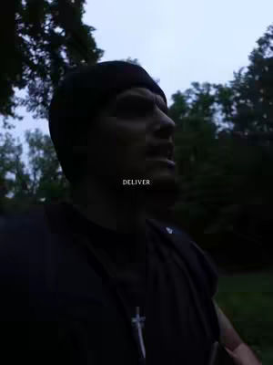 A man wearing a black beanie and a dark t-shirt with a cross pendant is looking up and to the right, with a forest background. The word "DELIVER" is overlaid on the image.