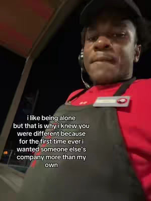 A medium shot shows a Black man in a red shirt and a black apron, against a dimly lit background. Text overlays the image. The man is looking towards the camera with a neutral expression.