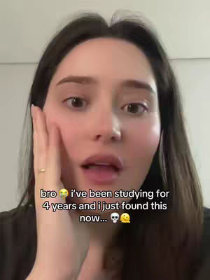A selfie-style video cover image featuring a young woman with long dark hair, looking directly at the camera with a surprised expression. Her right hand is raised to her cheek, and text overlays appear below her face. The background is a plain, light-colored wall.