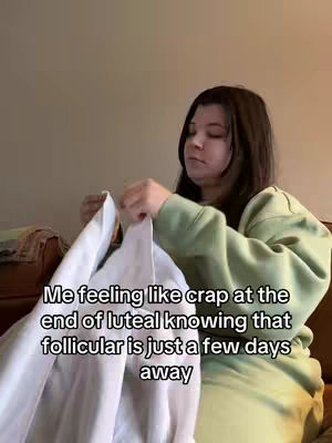 A woman with long dark hair and a green sweater is holding up the corner of a white blanket in front of her, with text overlayed on the scene.