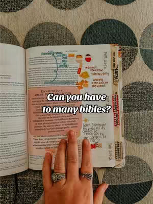 The image shows an open Bible with annotations and colorful sticky notes resting on a patterned surface. A hand with rings is partially visible.