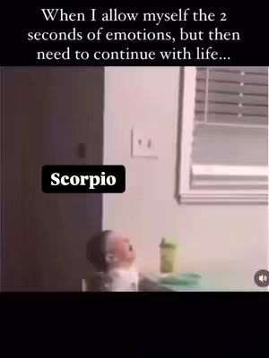 The image shows a baby crying, seated in a high chair with a table in front, and a window with a white frame in the background against a light brown wall. A text overlay with the word "Scorpio" is placed in a black box on the lower-left corner of the image, a green cup is visible on the table.