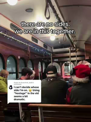 The video shows the interior of a trolley with people seated, some wearing winter attire and Santa hats, suggesting a holiday outing. The lighting is warm, and the focus is on the passengers, with an overlay of text. It is a scene from inside a trolley car, featuring passengers. The lighting is dim, with overhead lights illuminating the scene. The color palette leans towards warmer tones due to the interior and exterior lighting.