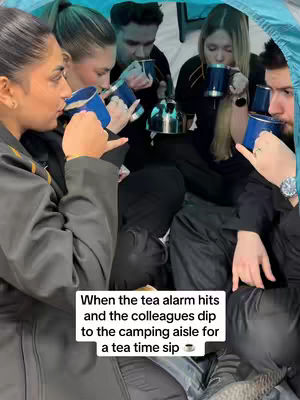 The image shows a group of people, mainly women, inside a camping tent. They are all holding mugs and appearing to drink from them. The setting is a dimly lit interior, possibly a pop-up tent, with a kettle visible, suggesting they are making tea. The composition is an eye-level medium shot emphasizing the group activity, with the text overlayed on the bottom.