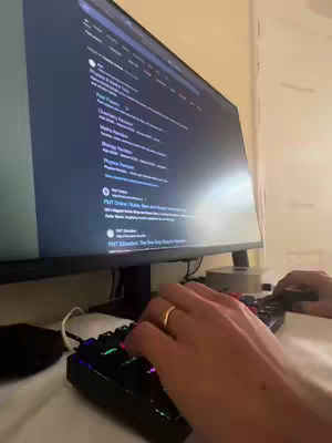 A person's hands typing on a keyboard with a monitor displaying a webpage in the background, likely related to a study app. The scene has a low-angle perspective.