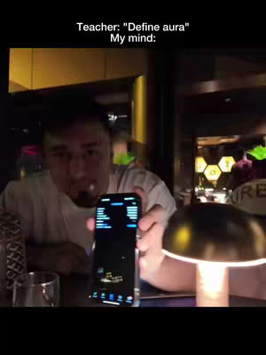A man sitting at a table in a dimly lit bar, holding a smartphone and looking towards the camera. On the screen, financial charts are displayed. The background has a warm color palette.