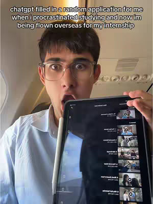 A young man with short dark hair and glasses is holding a tablet, looking directly at the viewer with a surprised expression. His mouth is open as if gasping. The image is taken from a slightly low angle, suggesting he is on a plane, as the interior ceiling is visible behind him; The text overlay on the top of the image reads: "chatgpt filled in a random application for me when i procrastinated studying and now im being flown overseas for my internship"