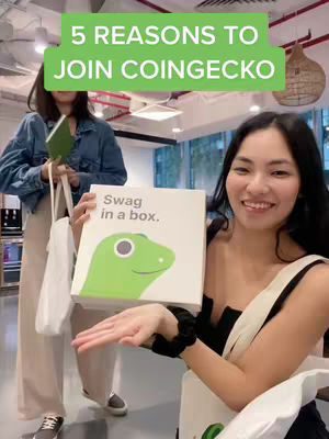 Two women are in an office setting. The focus is on a woman holding a white branded box with a green gecko logo and the words 'Swag in a box.' A green rectangular text above the women says '5 REASONS TO JOIN COINGECKO'. The other woman in the background is holding a notebook and a bag.