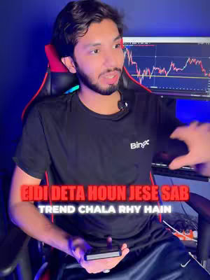 A man with dark hair and a beard sits in a gaming chair in front of a computer screen displaying what appears to be a stock chart. The man is wearing a black t-shirt and is holding a smartphone. Overlayed on the image in a red gradient is the text "EIDI DETA HOUN JESE SAB" and "TREND CHALA RHY HAIN."