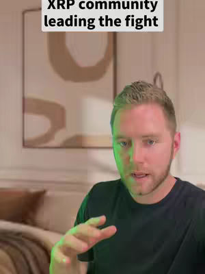 A man is talking to the camera, with a text overlay at the top that reads 'XRP community leading the fight'. The background includes an abstract painting and a blurred bedroom setting.