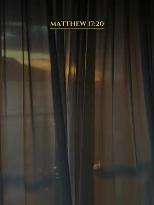 The image shows a blurred view through a sheer curtain. Vertical lines of the curtain are visible, along with a soft, warm light illuminating the background. The text 'MATTHEW 17:20' is overlaid at the top.