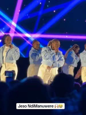 The image is a group of women on a stage, performing with microphones. They are dressed in light blue jean jackets and white pants. The background is a stage with purple and blue lights. At the bottom of the image, text reading "Jeso NdiManuwere" is displayed in a white box, along with some emojis.