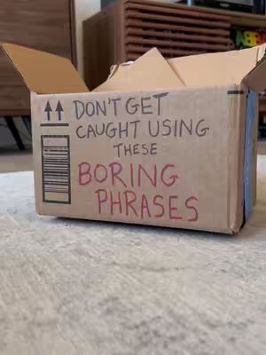 The image features a cardboard box with visible text written on it. The box is positioned on a textured surface, possibly a carpet or rug. The background is blurred.