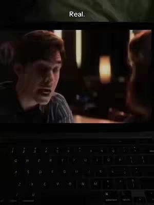 The cover image is a darkened shot of a laptop screen. On the screen, a scene from a movie or video is playing, showing a man in a striped shirt speaking. The scene is dimly lit, giving it a serious or dramatic feel. Above the screen there is a dark area, and the hook 'Real.' is written.