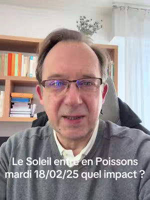 A middle-aged man with glasses and a grey sweater is centered in the frame, speaking directly at the camera. He is in front of a bookshelf filled with books. Text overlayed at the bottom of the screen reads in French.