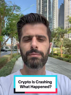 A man with a beard stands outdoors, the focus is on his face with a background of greenery and tall buildings. He is wearing white earphones and a white t-shirt. The text overlay at the bottom of the image says 'Crypto Is Crashing What Happened?'.