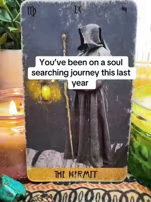 A tarot card, 'The Hermit', is the main focus. It depicts a hooded figure holding a lantern and staff. The card is set against a dark, textured background. In the background, there are candles.