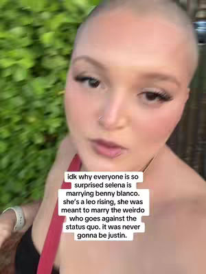 The cover image features a close-up of a bald woman looking directly at the camera, with a slight smile evident. Her face is softly lit, with pronounced makeup, including long eyelashes, blush, and lip color. A red strap can be seen on her shoulder, suggesting she is wearing a top. The background is a blurred, green foliage, indicating an outdoor setting. Overlayed text fills a white rectangle, providing a caption.
