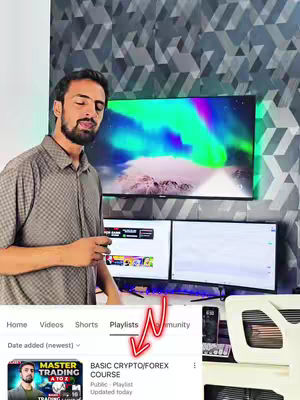 A man stands in front of a computer setup with two monitors and a large TV displaying colorful graphics. A red arrow points to a playlist highlighted on the screen, indicating a basic crypto/forex course.