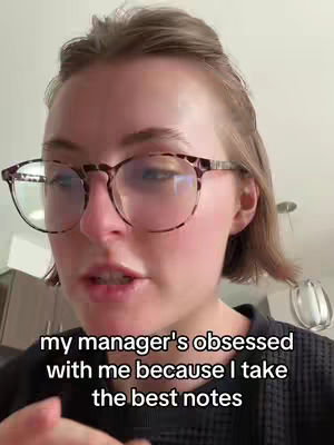 A selfie-style video, the creator is a woman with short brown hair, wearing round glasses. The background is minimal, with the upper kitchen cabinet visible.