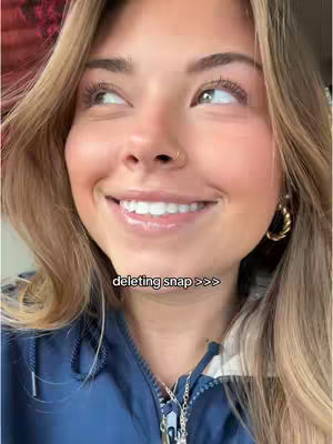 A close-up shot of a young woman smiling and looking upwards. She has long blonde hair, a nose ring, and is wearing a dark blue jacket. The text overlay reads "deleting snap >>>".