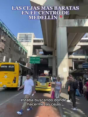 The image captures a street scene in Medellin, Colombia. The foreground features a man walking across a crosswalk. A yellow bus and a yellow taxi are prominent, and there are pedestrians walking in the background. The text overlay indicates that the content is related to eyebrow services.