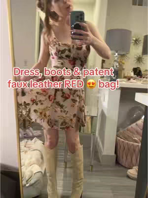 A woman is standing in front of a mirror, holding a phone, wearing a floral dress, cream-colored boots, and the image has a text overlay.