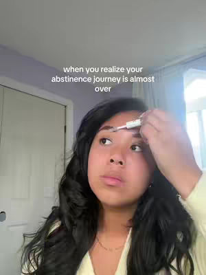 The cover image shows a young woman in a close-up shot, mid-action. She has long, dark, wavy hair and is looking upward with a focused expression. The background is soft, and there is text overlaid on the image. She is holding a makeup applicator near her eyebrow. The lighting appears natural, and the overall composition is casual and direct.