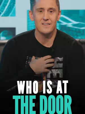 A medium shot shows a man with short brown hair, centered in the frame. He wears a black sweater with a design on the chest and is posed with his left hand over his heart. Bold white text, 'WHO IS AT THE DOOR' covers the lower half of the image.