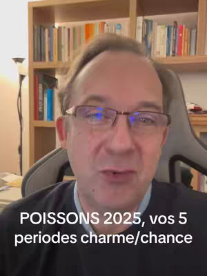 A middle-aged man with glasses is centered in front of a bookcase filled with books. The man is wearing a dark top and facing toward the camera, speaking. The image is well-lit and the background gives context to the speaker. An overlay at the bottom of the screen displays text in white, setting the video's context.