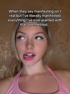 A close-up shot of a young, light-skinned woman with blonde hair and a pink top looking to the side with a slightly open mouth. Her tongue is visible, and the background is blurred, showing a textured pattern.