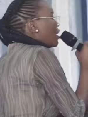 The cover image shows a close-up of a Black woman speaking into a microphone. She is wearing glasses and has her hair styled in braids. She has an open mouth, suggesting speech or singing. The background is slightly blurred, with some light and shadow play.