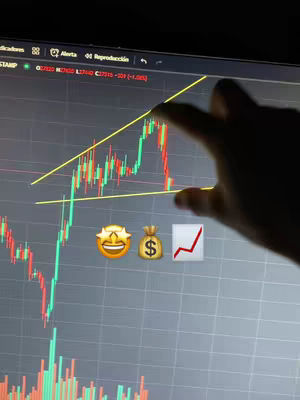The image shows a computer screen displaying a stock chart with red and green candlesticks. A hand is pointing towards a rising trend line drawn in yellow. Emojis representing a grinning face with stars, a money bag, and an upward-trending graph are placed below the chart. The screen's background is dark.