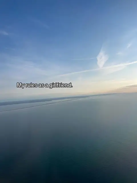 The cover image depicts a tranquil aerial view over a vast expanse of water, likely an ocean or a large lake. The sky is primarily a soft, muted blue, with streaks of clouds at the top and edges. The text overlayed on the image reads 'My rules as a girlfriend'.