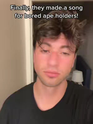 A man with dark hair is centered in the frame. Text overlay is visible at the top with the text "Finally, they made a song for bored ape holders!". The man has a serious expression, looking downward slightly. The background is blurred.