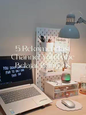 The image showcases a well-lit workspace with a laptop displaying motivational text, a pegboard with stationery, and a desk lamp. The overall aesthetic is clean and modern.
