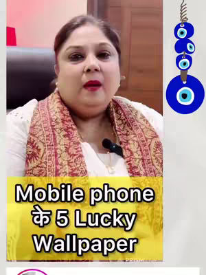 A woman with brown hair and red lipstick is centered in the frame, looking upwards slightly. She wears a white top and a patterned shawl, and a small microphone is clipped to her neckline. The background shows a wooden cabinet. A yellow rectangular box with bold, white text overlays the bottom, reading "Mobile phone के 5 Lucky Wallpaper". To the right, a string of blue and white evil eye charms hangs, suggesting a theme of protection or luck.