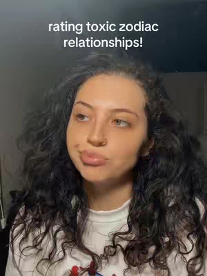 A woman with long curly dark hair, wearing a white shirt, is looking towards the left of the screen with a slight pout.