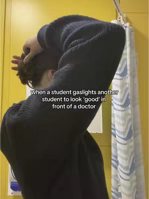 A person, viewed from the back, is adjusting their hair. They are wearing a dark blue sweater. The background has a yellow wall, with a striped shower curtain partially visible. Text is overlaid at the bottom, detailing a situation in a medical context.