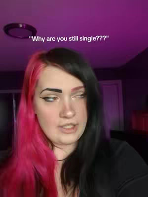 The cover image is a selfie-style shot featuring a young woman with pink and black split-dyed hair. Above her head is a text overlay that reads, "Why are you still single???". The background is a blurred interior space with dim purple lighting. The woman has a somewhat pensive expression, looking slightly off-camera.