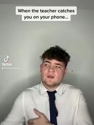 The image shows a young man in a white shirt and a dark tie, looking upward with a surprised expression. Above him, text reads, 'When the teacher catches you on your phone...'.
