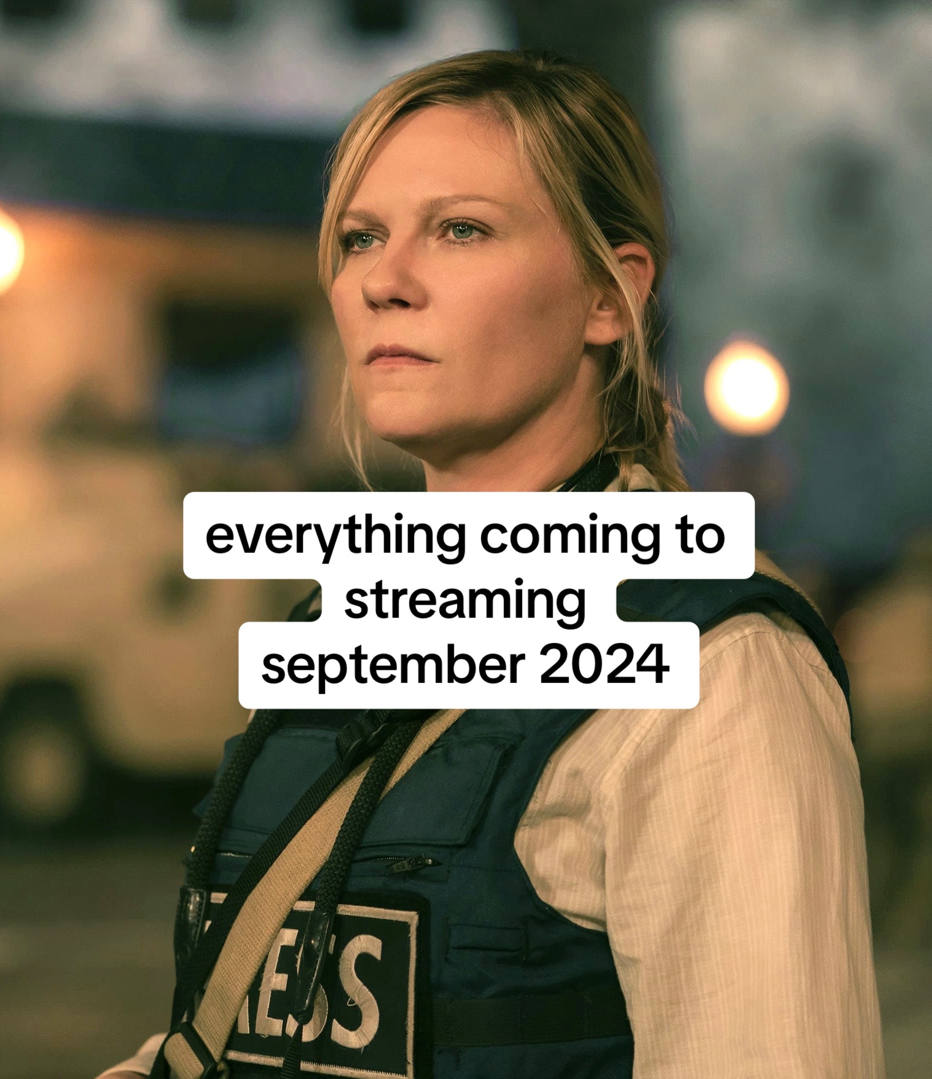 The image shows a woman looking off to the side with a serious expression. She is wearing a beige shirt and a dark blue vest that says "PRESS" in white letters. The background is blurred, with some lights visible, suggesting an outdoor setting. Text overlays in white boxes read "everything coming to streaming september 2024."