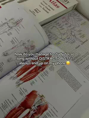 The image displays an open textbook with anatomical drawings, possibly muscles, overlaid with text. Other textbooks and notes partially visible in the background with written text.