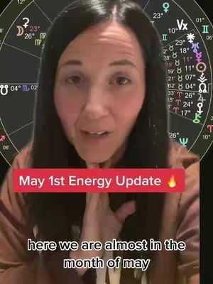 A woman with long dark hair is in the foreground, speaking to the camera. Behind her is a superimposed graphic of a zodiac wheel, with astrological symbols. Text overlays are present, including a banner that reads \"May 1st Energy Update\" in red text with a flame icon. Below, smaller text highlights the month of May.