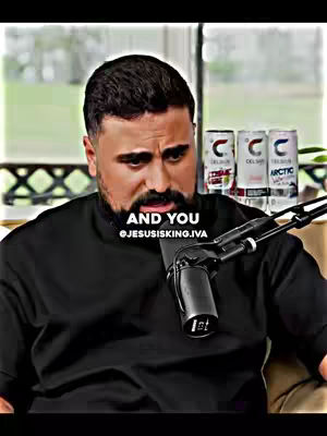 The image shows a man in a partially open, black collared shirt. He has a dark beard and short, dark hair. He is looking down, and a microphone is directly in front of him. Behind him, in the neutral background, are three cans of beverage. Text overlays near the bottom of the image say "AND YOU" and "@JESUSISKING.IVA".