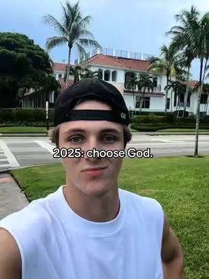 A young man wearing a black baseball cap and a white tank top stands in front of a large house with palm trees and a clear blue sky. Text on the image reads \"2025: choose God.\"